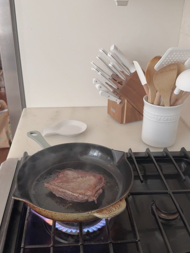 Sizzling skirt steak cooking in a cast iron skillet, showing a perfect sear and juicy texture – protein-packed recipe by megannashhealth.