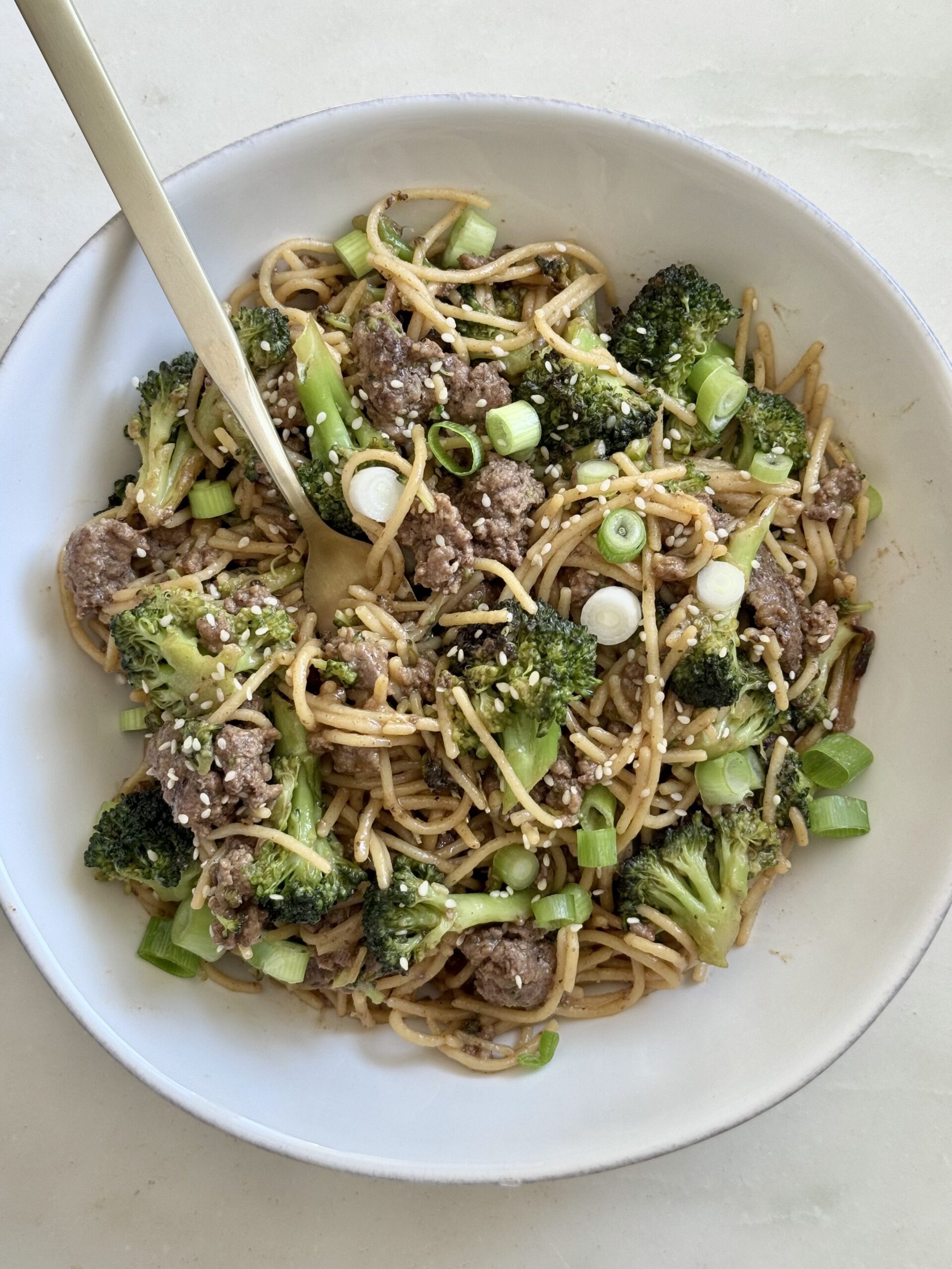 Overhead shot of spicy beef and broccoli stir fry with Banza noodles in a large white bowl