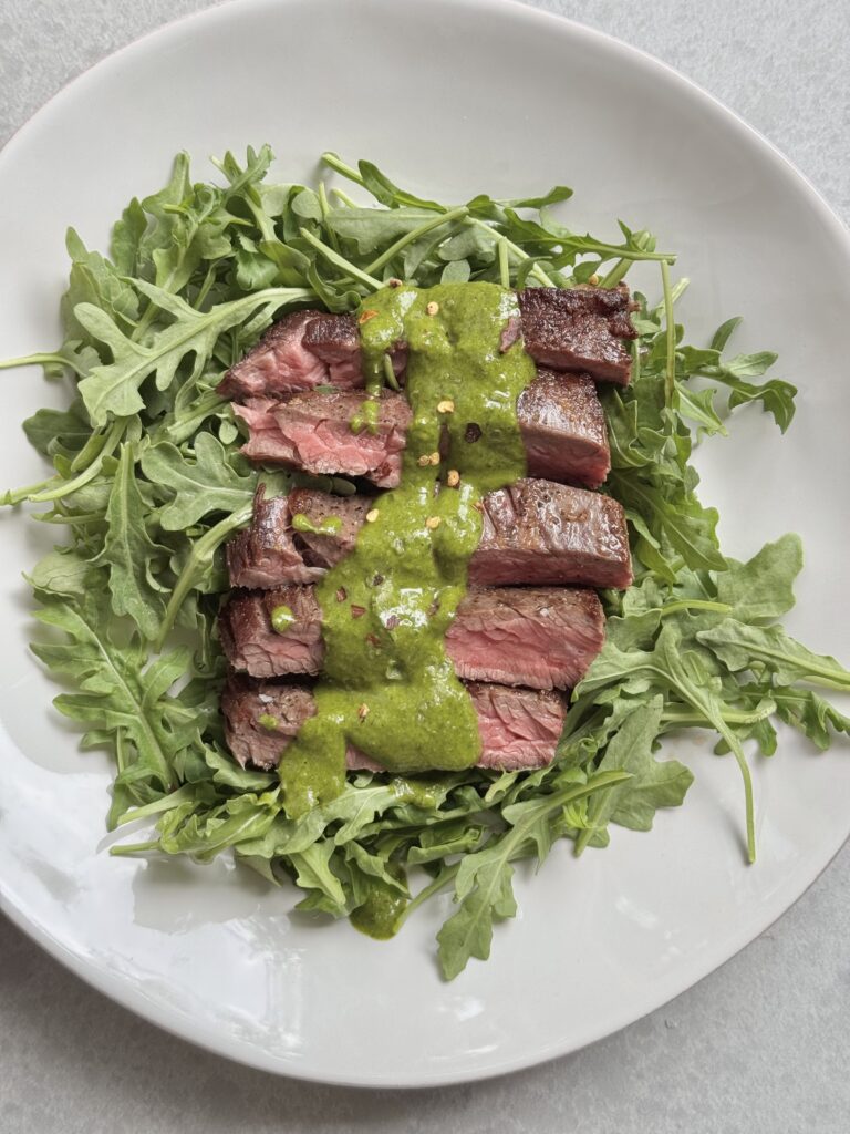 Close-up of juicy cast iron-seared skirt steak served with vibrant chimichurri – healthy and fast meal by megannashhealth.