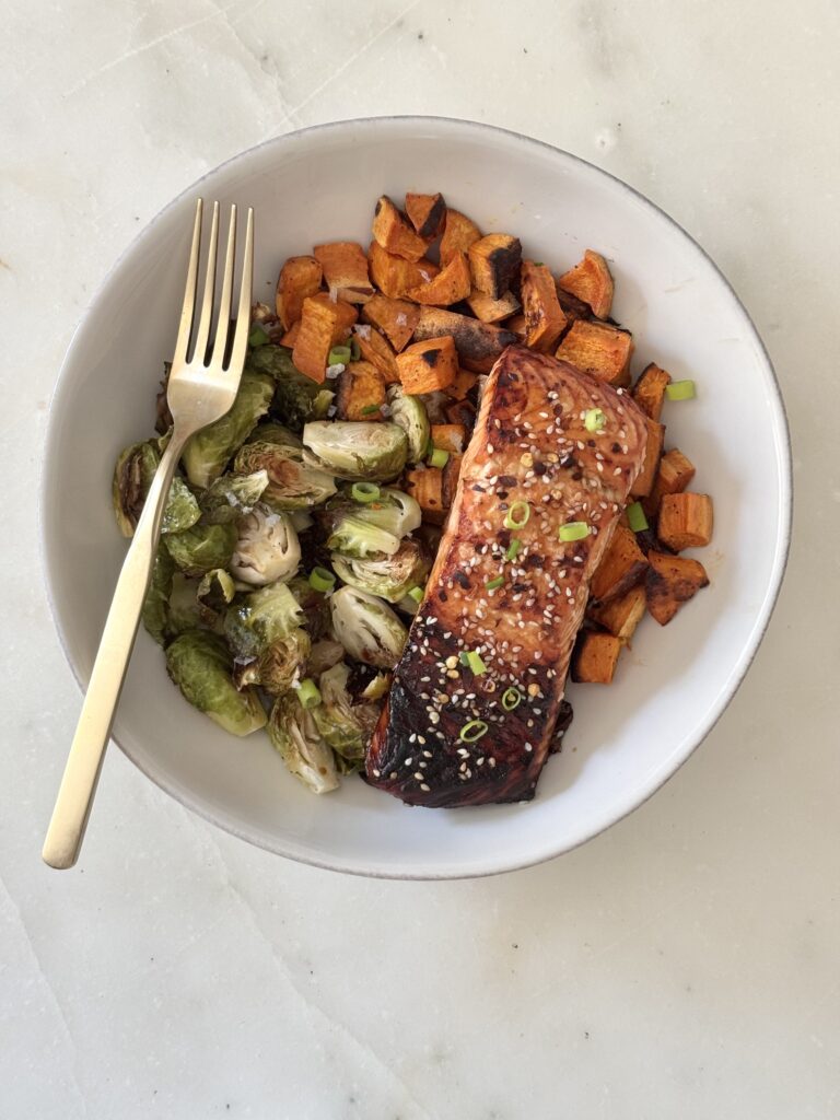 A perfectly cooked Ginger Soy Salmon fillet, plated and drizzled with a rich tamari-based glaze. This gluten-free and high-protein dish is served alongside a vibrant mix of roasted vegetables, making it a wholesome and satisfying meal for any occasion.