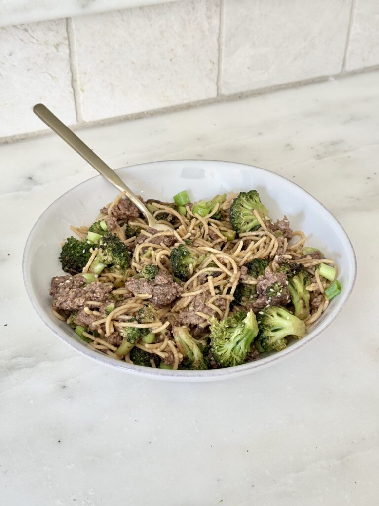 Close-up of glossy coconut amino sauce coating noodles, beef, and broccoli