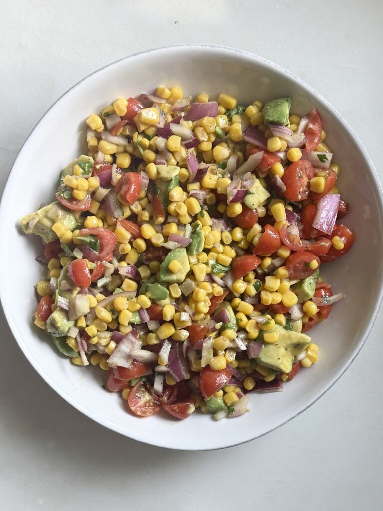 Overhead shot of chopped cherry tomatoes, avocado, corn, red onion, and cilantro — colorful whole food ingredients for a healthy salad.