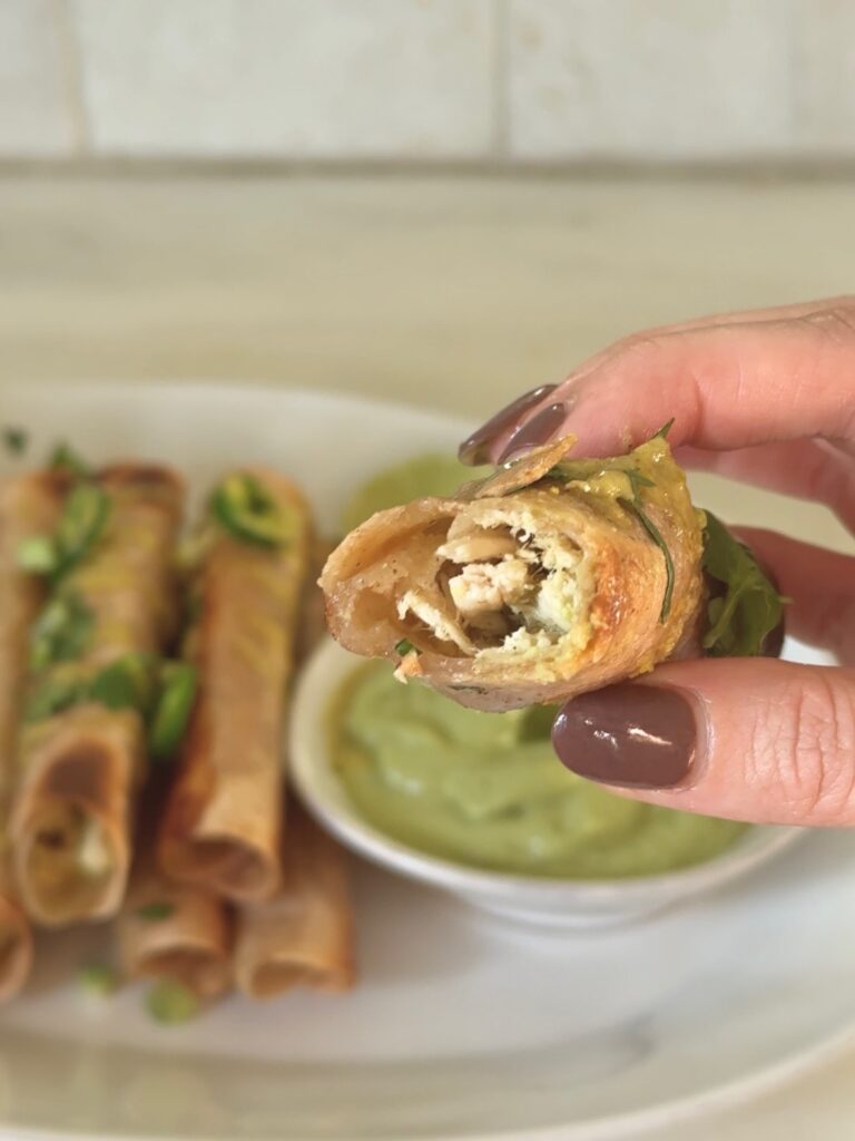 Close-up of a chicken taquito with a bite showing the shredded chicken filling