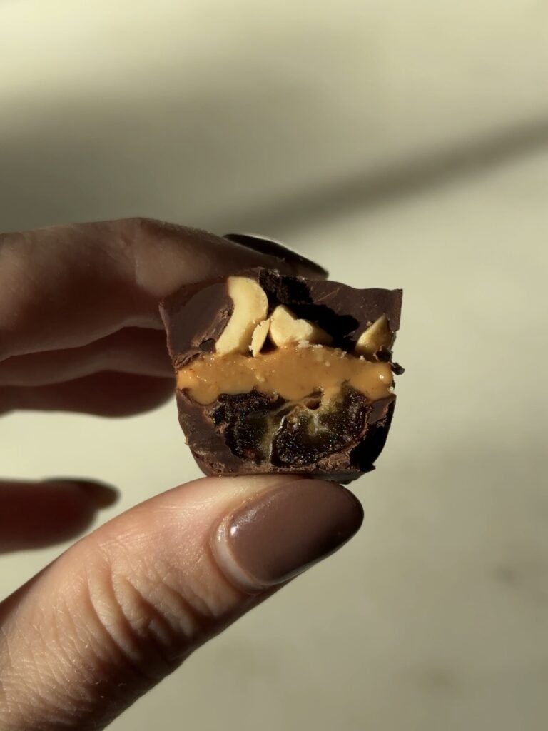 Close-up of a vegan Mini Snickers bite with a piece missing, revealing the chocolate, date, and peanut butter layers.