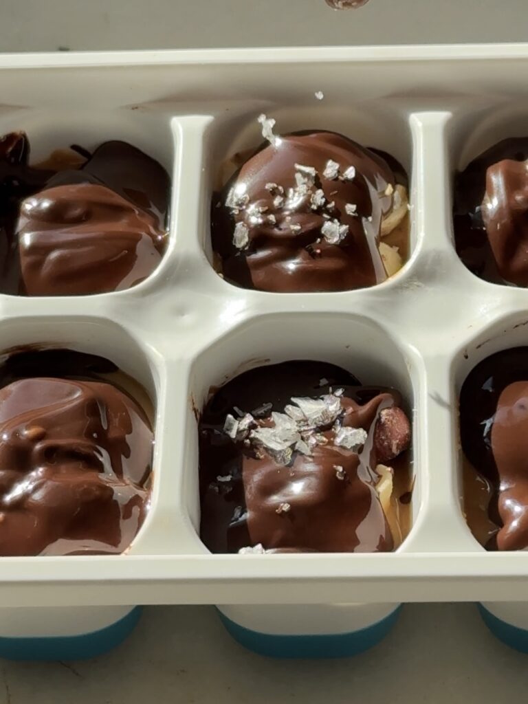 Pouring flaky sea salt over vegan Mini Snickers bites in a mold, highlighting the sweet and salty topping.