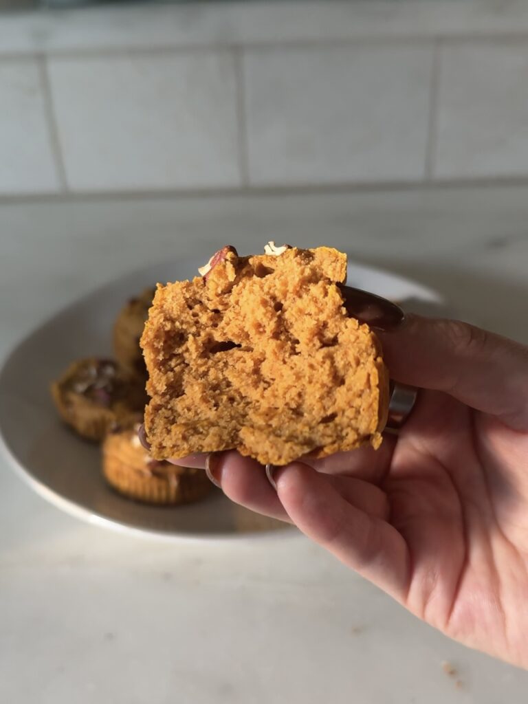 Close-up of a gluten-free pumpkin protein muffin with a bite taken, showing the soft, fluffy texture and moist interior