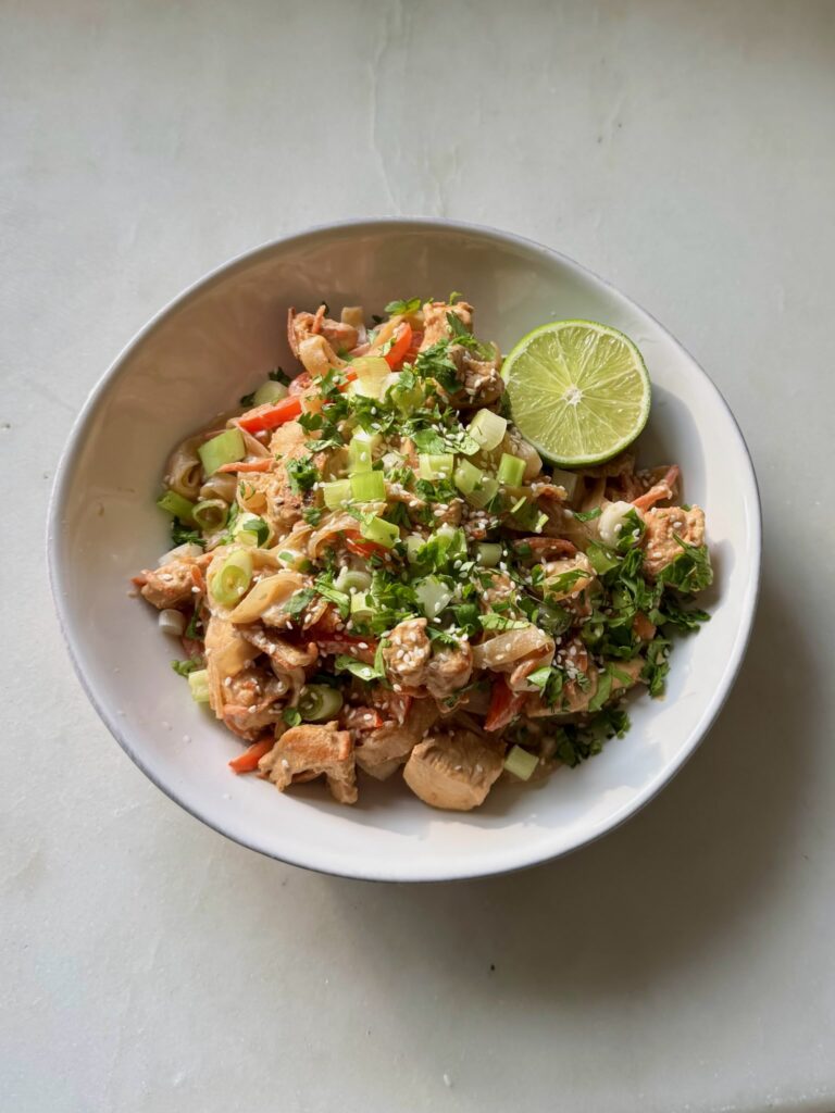Close-up of low-carb Tahini Chicken Pad Thai served in a white bowl with green onion and cilantro