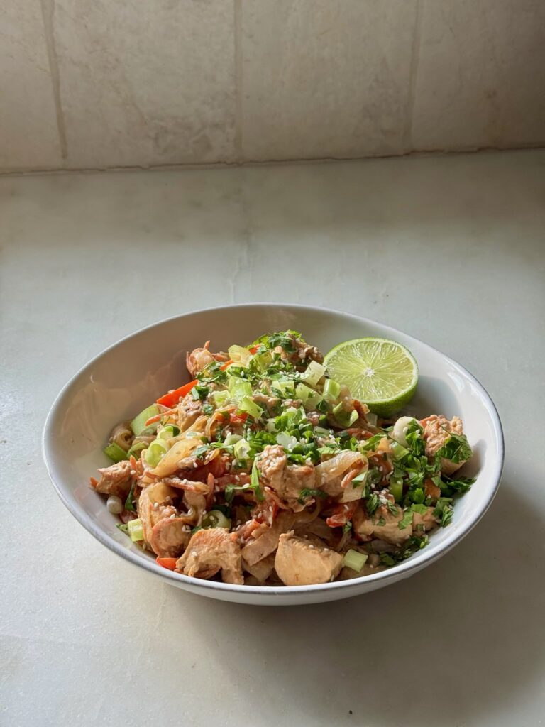 Completed Tahini Chicken Pad Thai in a bowl, garnished with sesame seeds and fresh herbs
