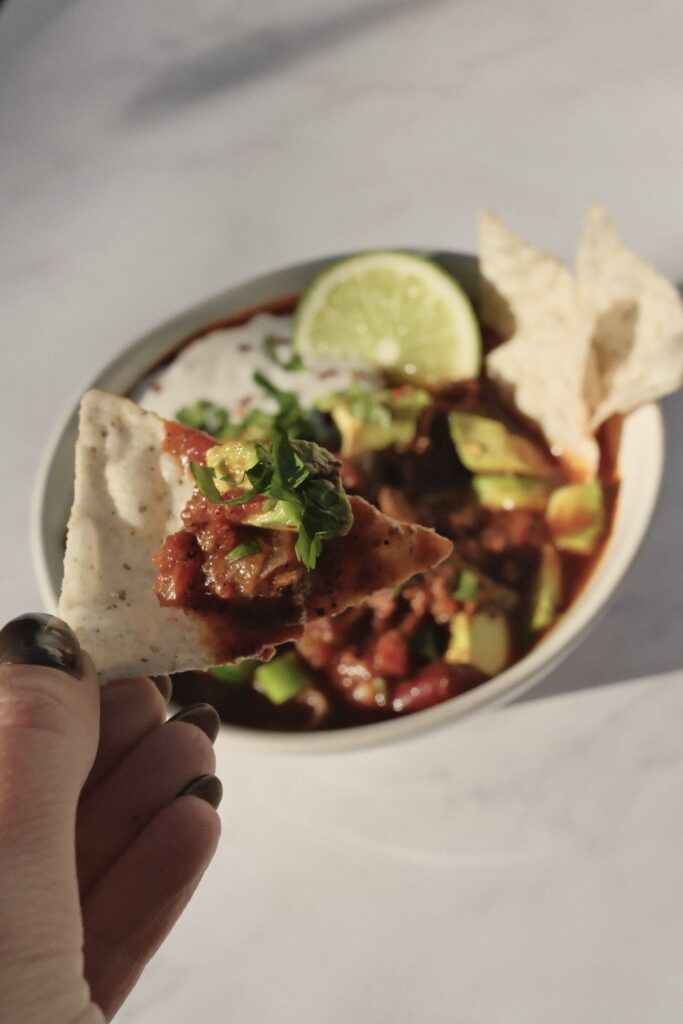 Tortilla chip dipped into thick, tomato-based beef chili.