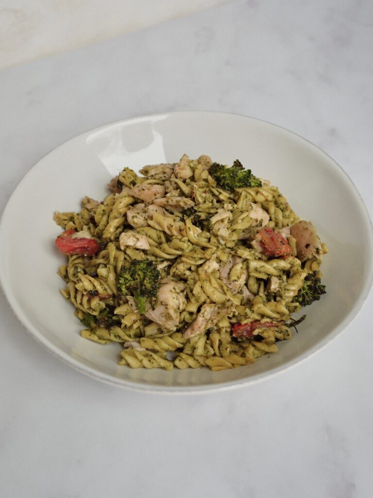 Bowl of gluten-free pesto chicken pasta topped with lemon zest, parsley, and red pepper flakes.
